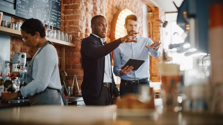 Business coach advising small business owners on efficient operations in a cafe.